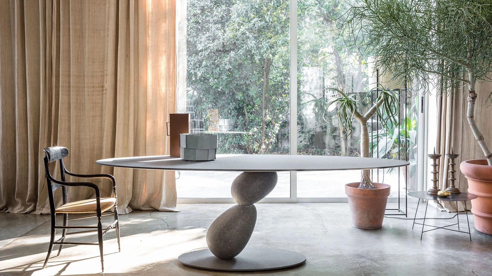 Tavolo ovale con struttura in metallo e piano in MDF rivestito con finiture materiche con due sassi che sorreggono il piano Matera di Mogg